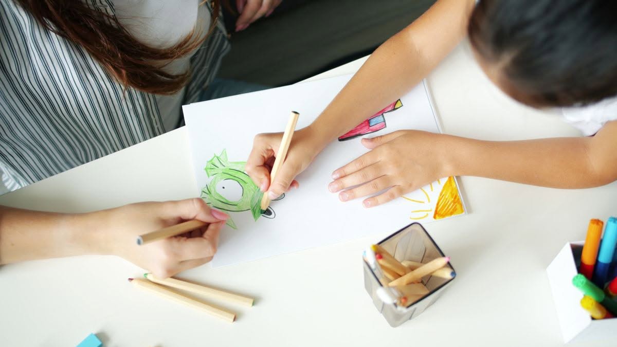 Logopedista e bambino disegnano insieme al tavolo durante un'attività sul linguaggio